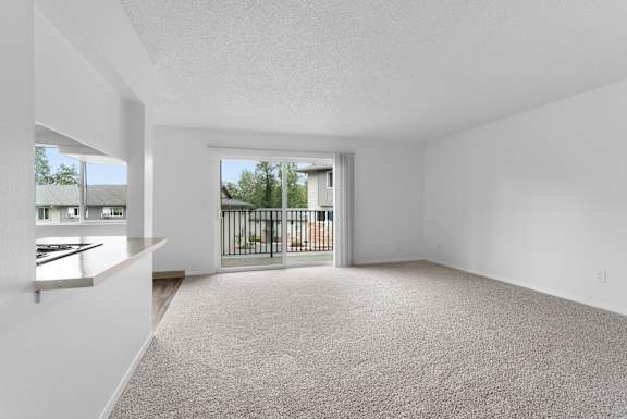 A spacious, empty room with a carpeted floor and a view of a balcony with a railing.
