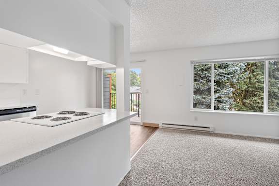 A white kitchen with a stove top oven and a window with a view of trees.