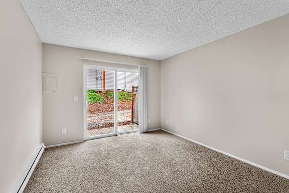 A room with a carpeted floor and a sliding glass door leading to a backyard.