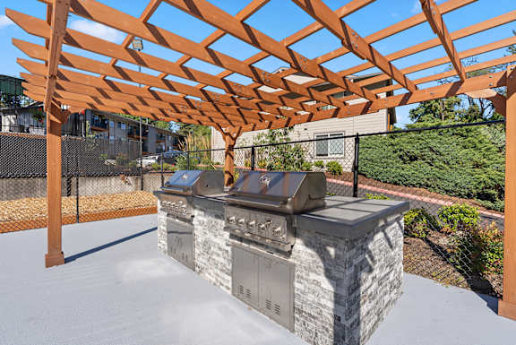 A wooden pergola is over a stone and metal grill.