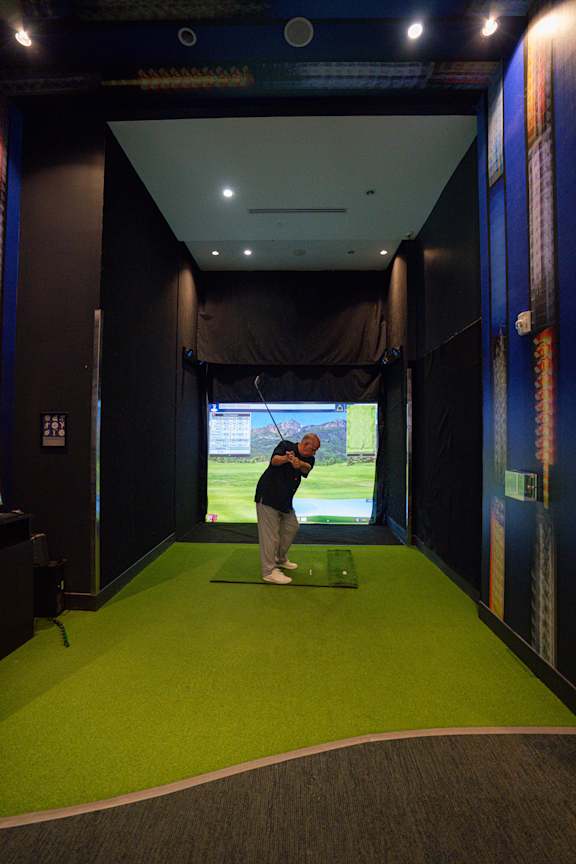 A man is playing golf in a room with a screen showing a golf course.