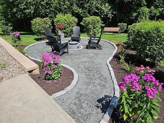 A garden with a circular concrete table surrounded by chairs and flowers.