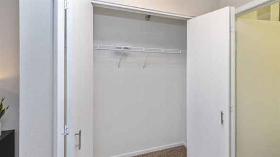A white closet with a coat hanger is open.