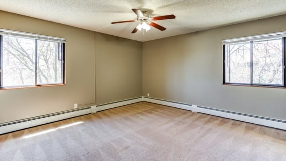A room with a ceiling fan and two windows.