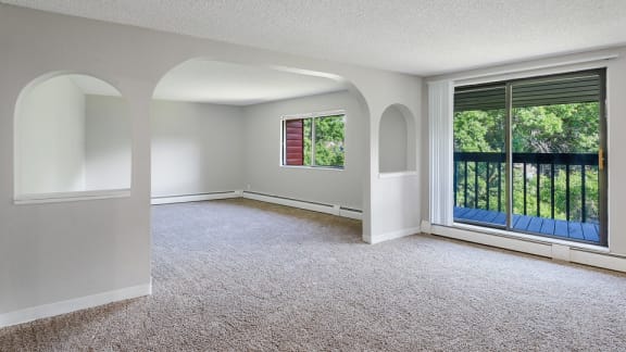 A room with carpeted floor and a window overlooking a balcony.