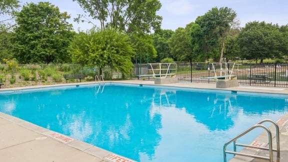 A large blue swimming pool surrounded by a metal fence and trees.