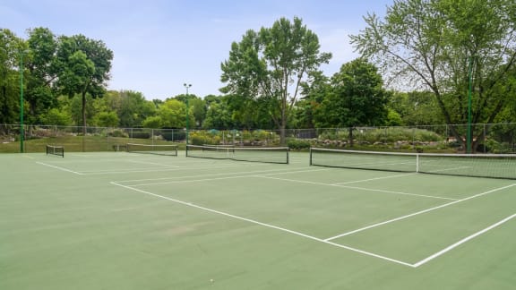 A tennis court surrounded by trees and a fence.