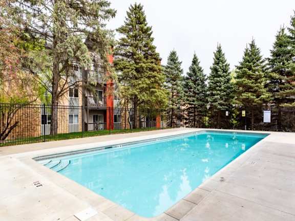 A swimming pool surrounded by trees and a building in the background.