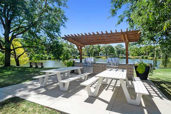 A wooden pergola shades a picnic table in a park.