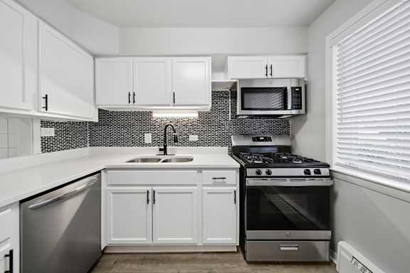 A kitchen with white cabinets and a black and white tiled backsplash.