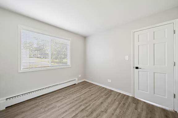 A room with a white door, window with blinds, and a radiator on the wall.