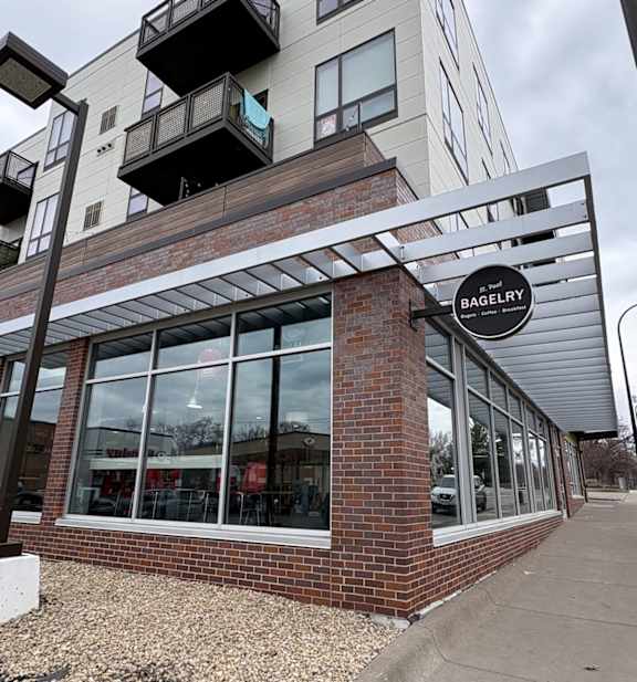 A Bagelry sign is mounted on a metal frame in front of a brick building.