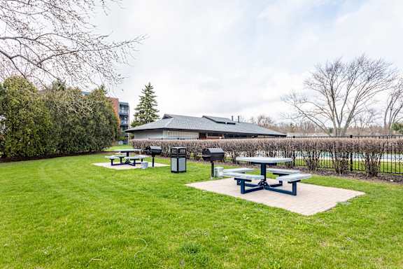 a group of picnic tables in a grassy area with a building in the background