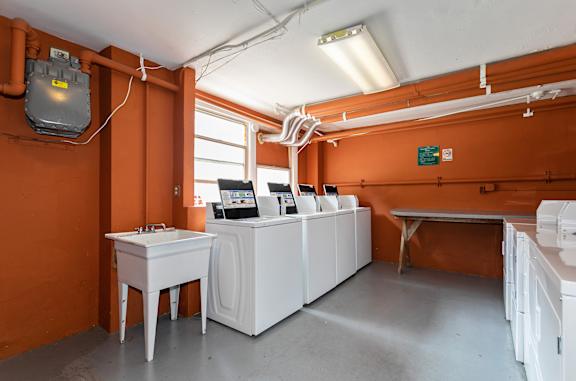 a laundry room with four washing machines and a sink at The Windham Apartments, Seattle, WA