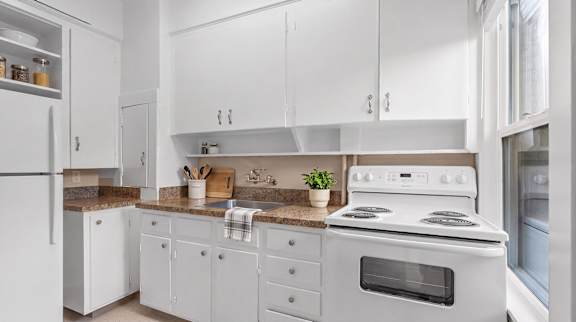 A white kitchen with a stove, refrigerator, and cabinets.