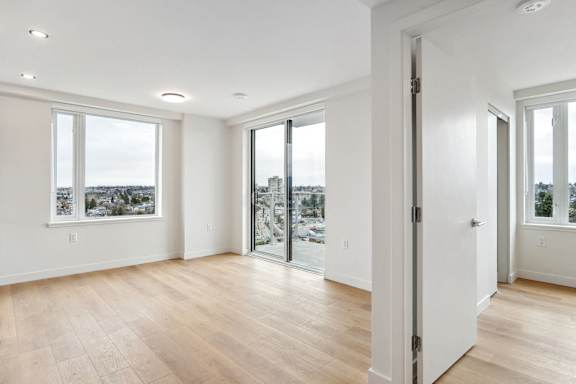 A room with white walls and wooden flooring with a view of a cityscape through the windows.