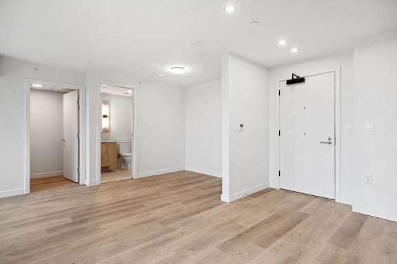A room with white walls and wooden flooring with a door on the right.