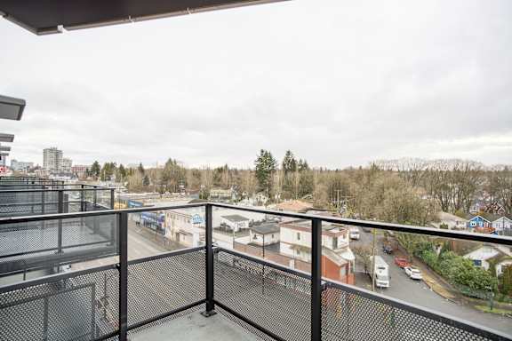 A balcony with a black railing overlooks a residential street.