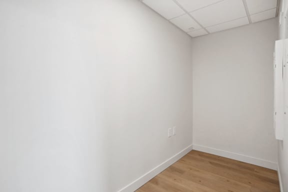 A white wall with a light switch and a wooden floor.