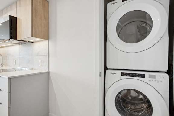 A white washing machine is stacked on top of a white dryer in a small laundry room.