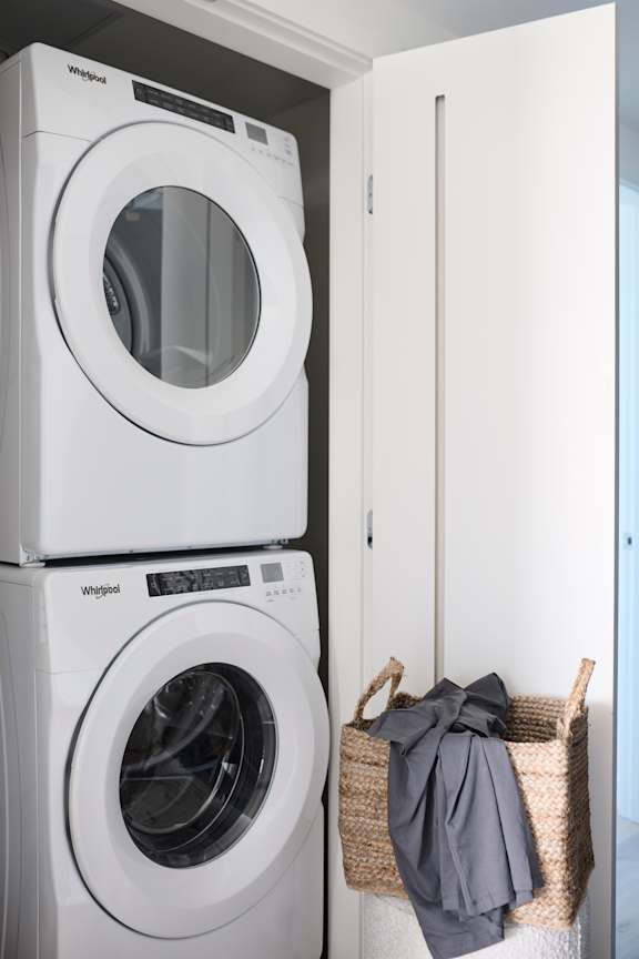 Two white Whirlpool washing machines stacked on top of each other in a laundry room.