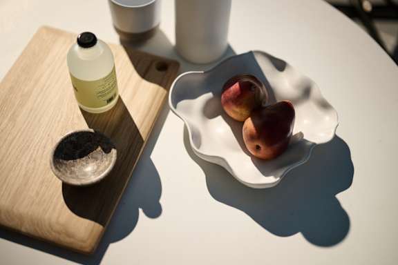 A bottle of oil, a small bowl of salt, and a plate of plums are on a table.