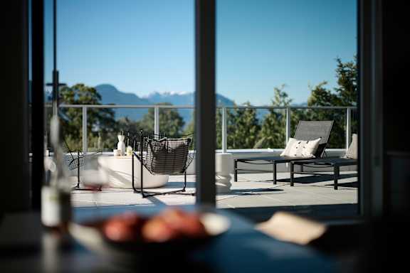 A table with a bowl of fruit on it in front of a window with a view of the mountains.