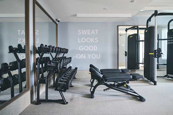 A gym with a mirror, weights, and a bench with the words "sweat looks good on you" on the wall.