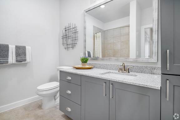 A bathroom with a white toilet, grey cabinets, and a marble countertop.