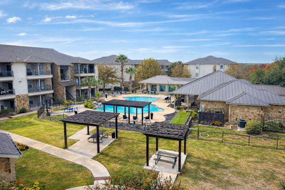 A large outdoor swimming pool surrounded by a black fence and a pavilion.
