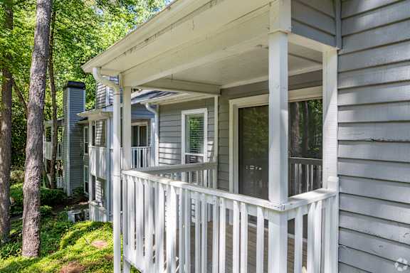A porch with a white railing and a grey house.