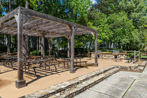 A wooden pavilion with a stone border is surrounded by trees.