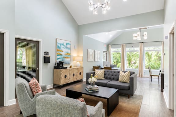 A living room with a grey couch, a grey armchair, a coffee table, and a painting on the wall.