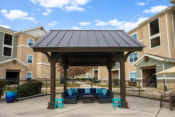 A gazebo with a black roof is surrounded by a black fence and blue couches.