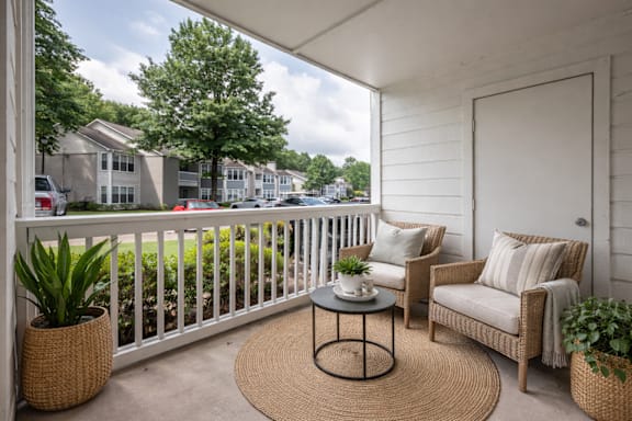 A patio with a white railing, a wicker chair, and a table with a plant on it.