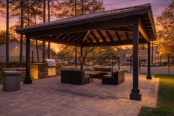 A pavilion with a stone floor and a roof is surrounded by trees.
