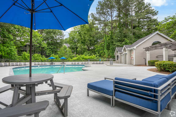 A blue umbrella is over a picnic table next to a pool.