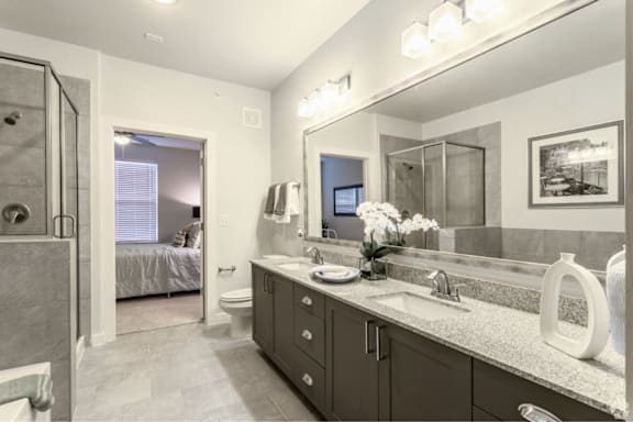 A bathroom with a sink, mirror, and a bed in the background.