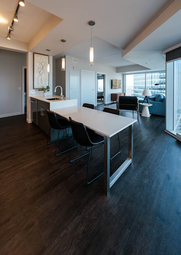 A modern kitchen with a long white table and black chairs.