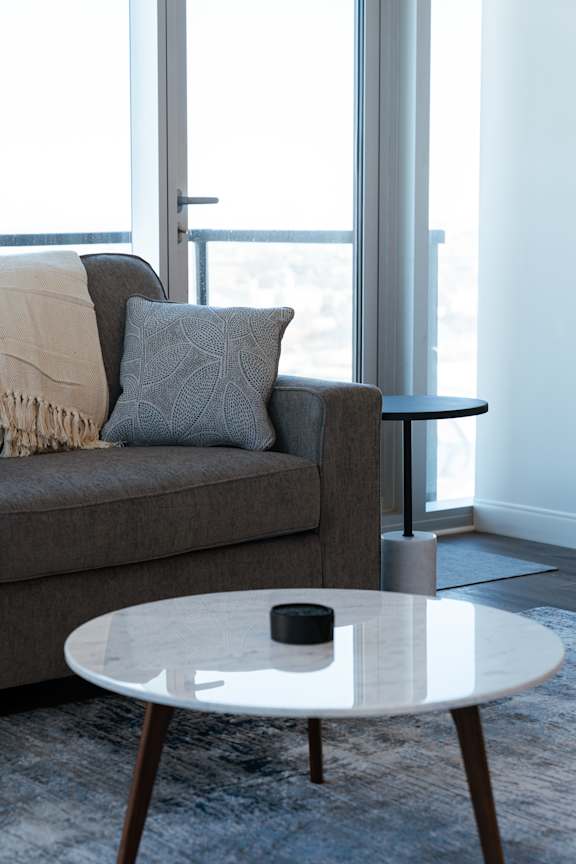 A modern living room with a grey couch, a white coffee table, and a large window.