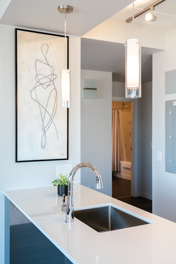A modern kitchen with a white countertop and a large abstract painting above it.