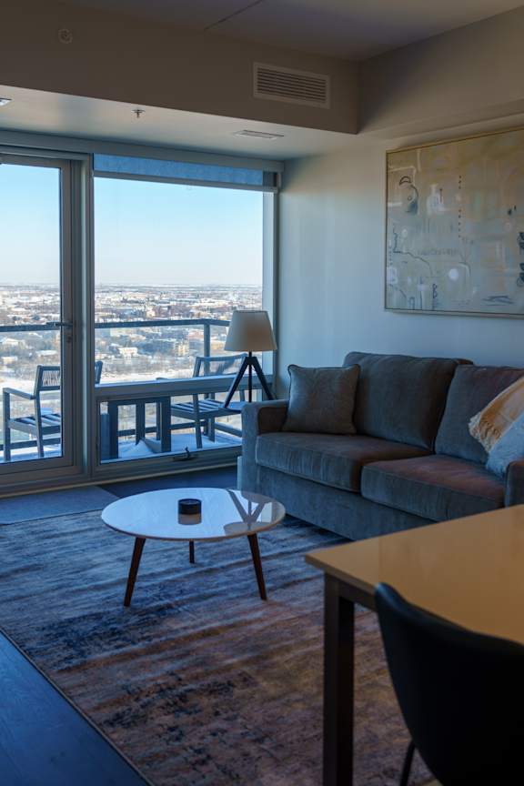 A living room with a grey couch, a white coffee table, and a large window overlooking a cityscape.