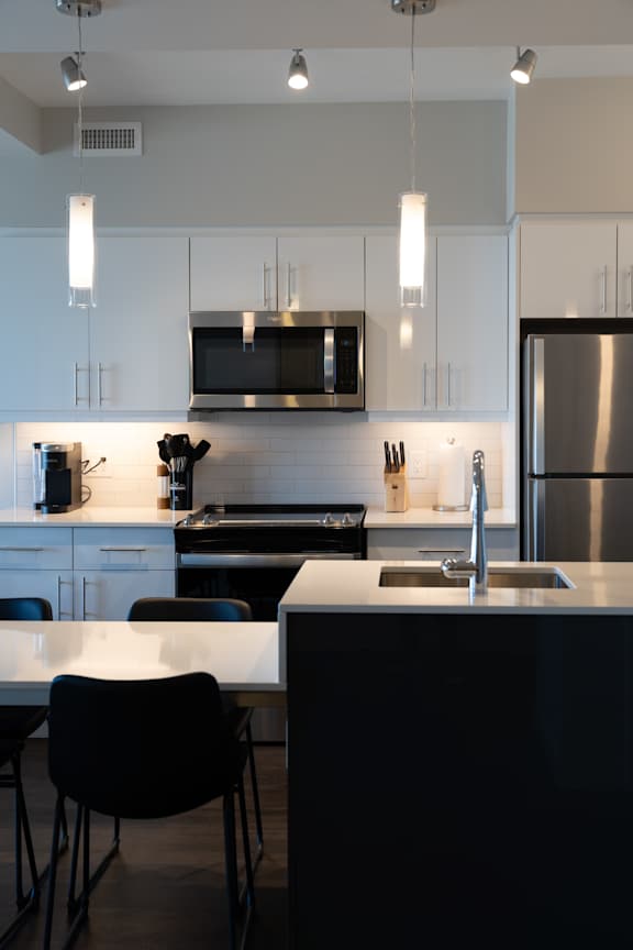 A modern kitchen with a stainless steel refrigerator and black chairs.