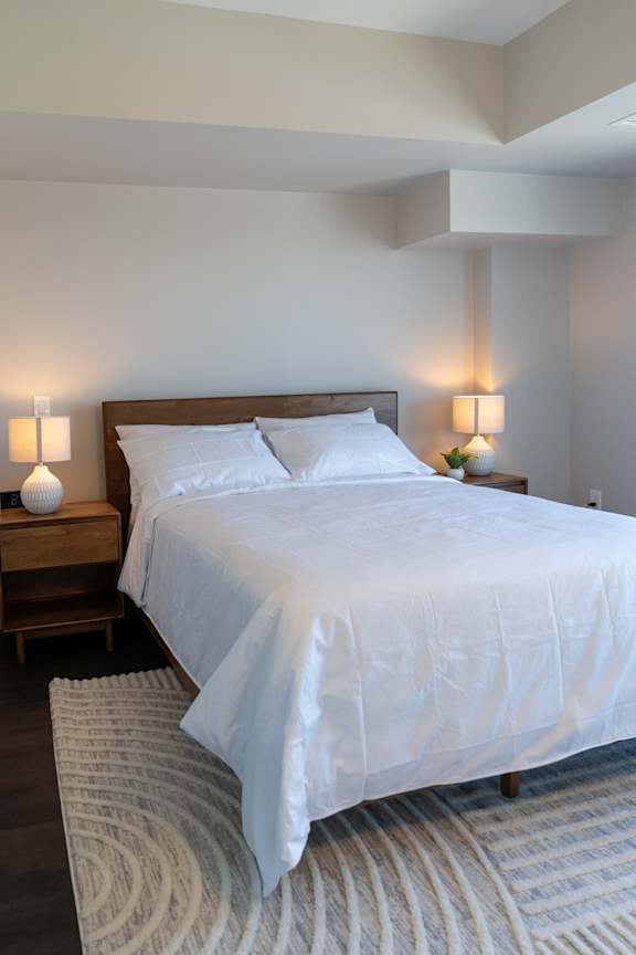 A bed with white bedding sits in a room with two lamps on either side of it.