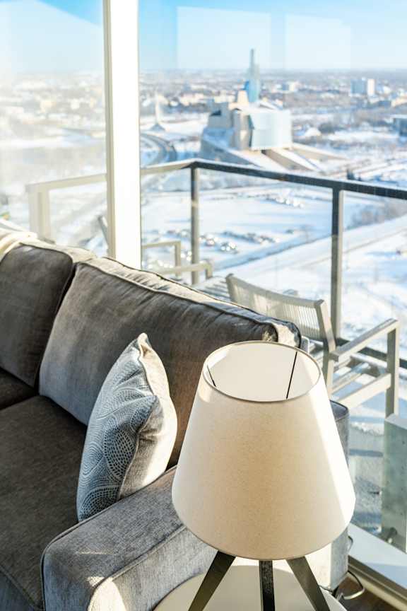 A lamp sits on a table in front of a grey couch.