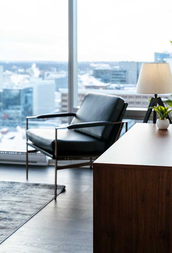 A black chair is placed in front of a window with a view of a cityscape.