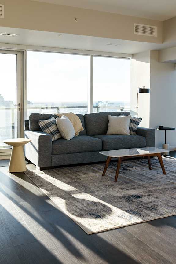 A grey couch with pillows and a small table in front of a large window.