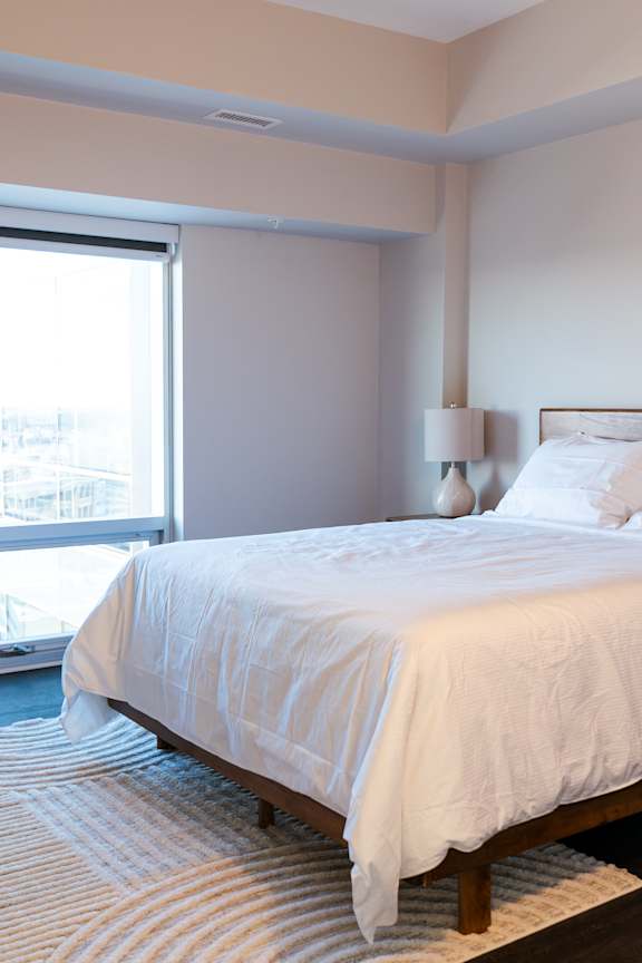 A bed with white bedding sits in a room with a striped rug.