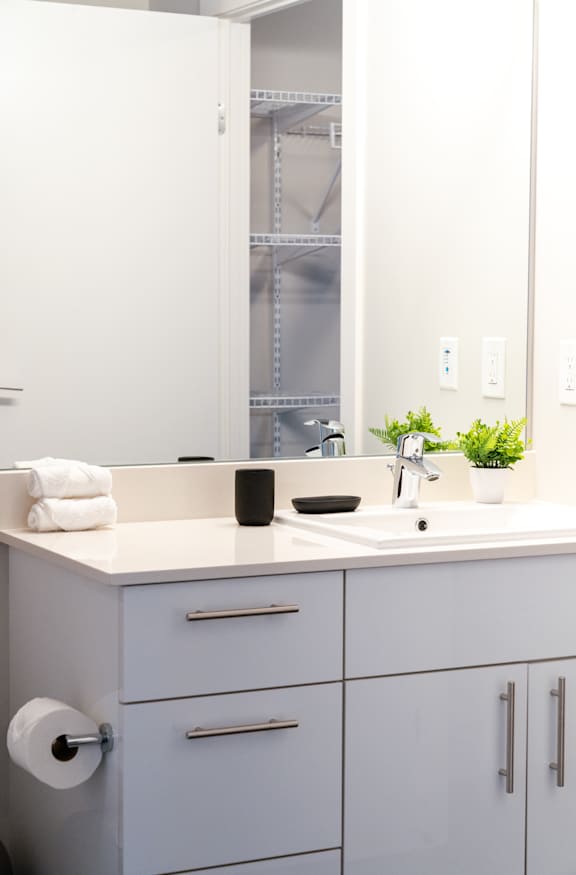 A white bathroom with a sink, mirror, and cabinets.