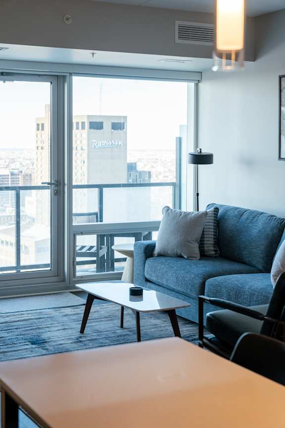 A living room with a blue couch and a table in front of a large window.